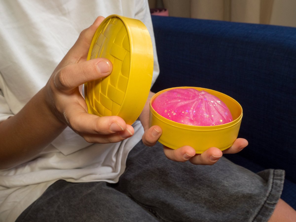 A child unboxing a pink glitter squishy dumpling toy from its packaging